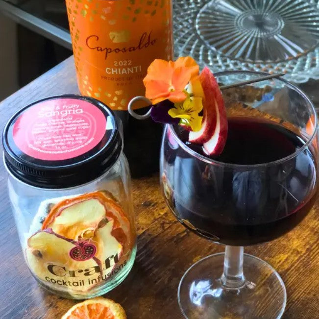 Glass of sangria next to a glass jar containing a sangria cocktail kit