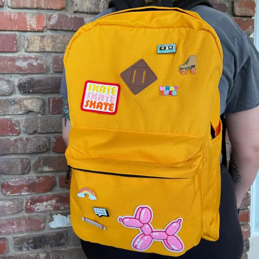 Yellow backpack covered in fabric patches and enamel pins