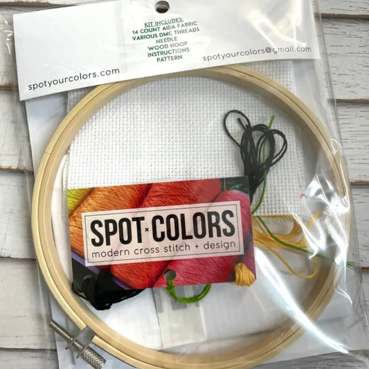 Embroidery hoop with cross stitch kit and 'Spot Colors' branding on a wooden surface