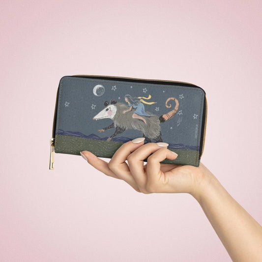 Hand holding a wallet with an illustration of a girl in a blue dress riding a giant possum