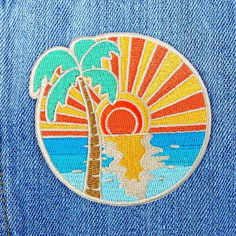 Embroidered fabric patch depicting a palm tree in front of an ocean sunset view