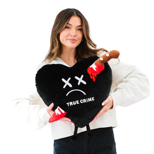 Large black heart plushie with x's for eyes and a bloody knife coming out either side. The words true crime are embroidered on it.