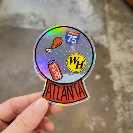 Hand holding holographic sticker shaped like a snowglobe with Atlanta iconic landmarks