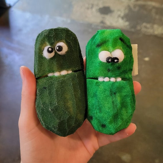Hand holding two green pickle foam puppets