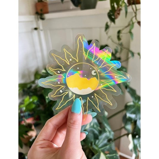 Hand holding Clear suncatcher sticker with colored yellow mountain and moon inside a flower