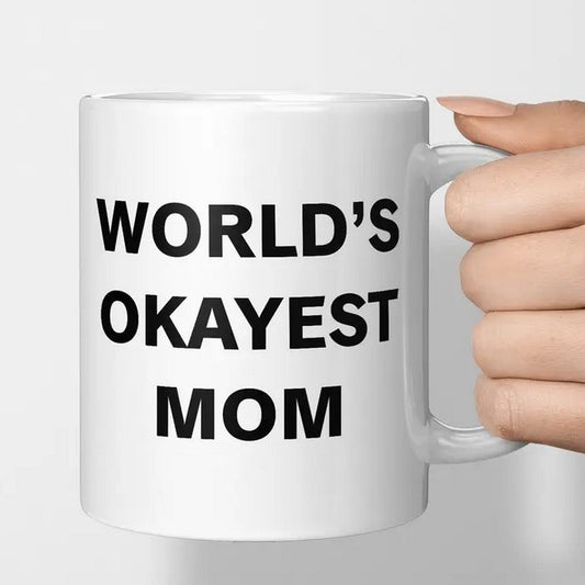 Hand holding black and white mug that says World's Okayest Mom