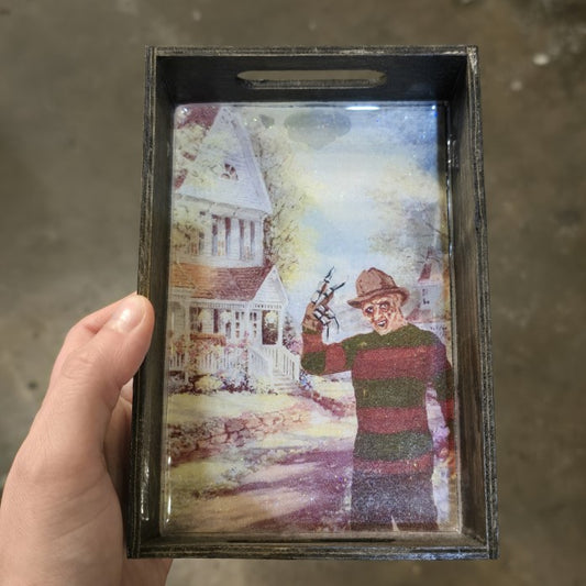 A small wooden tray with an image of Freddy Kreuger in front of a white Victorian style house.