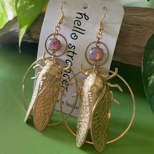 Gold dangle earrings shaped like cicadas with purple gemstones