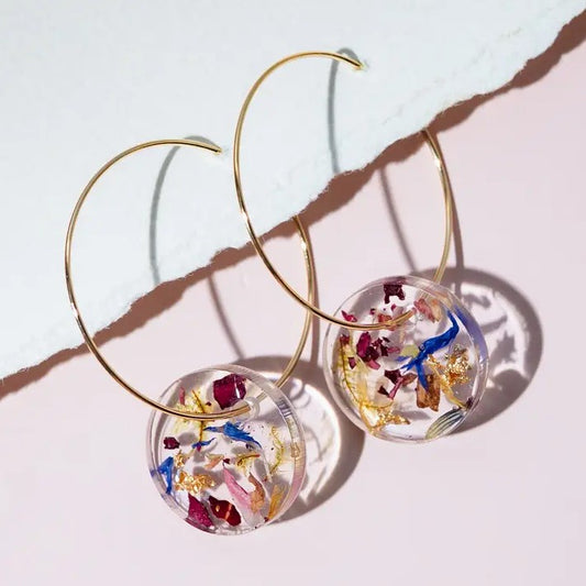 Gold hoop earrings with clear circular charms containing colorful dried flowers on a light background