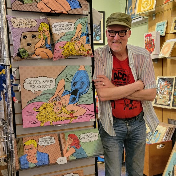 Artist Tom Heintjes of Bull Moose Publishing standing next to a display of his art prints and pillows
