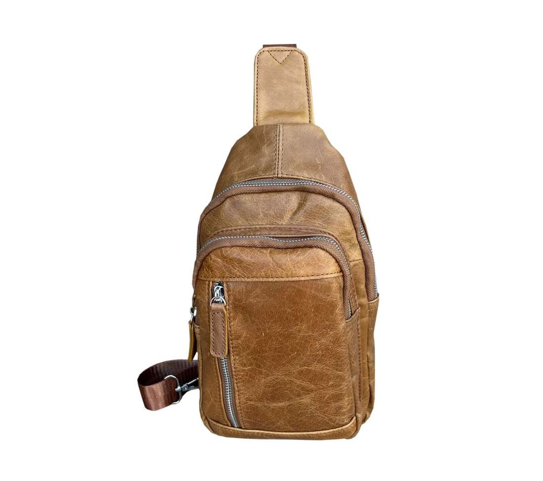 Front of a small tan leather crossbody bag with three zipper pockets on the front.