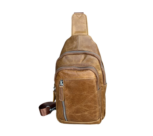 Front of a small tan leather crossbody bag with three zipper pockets on the front.