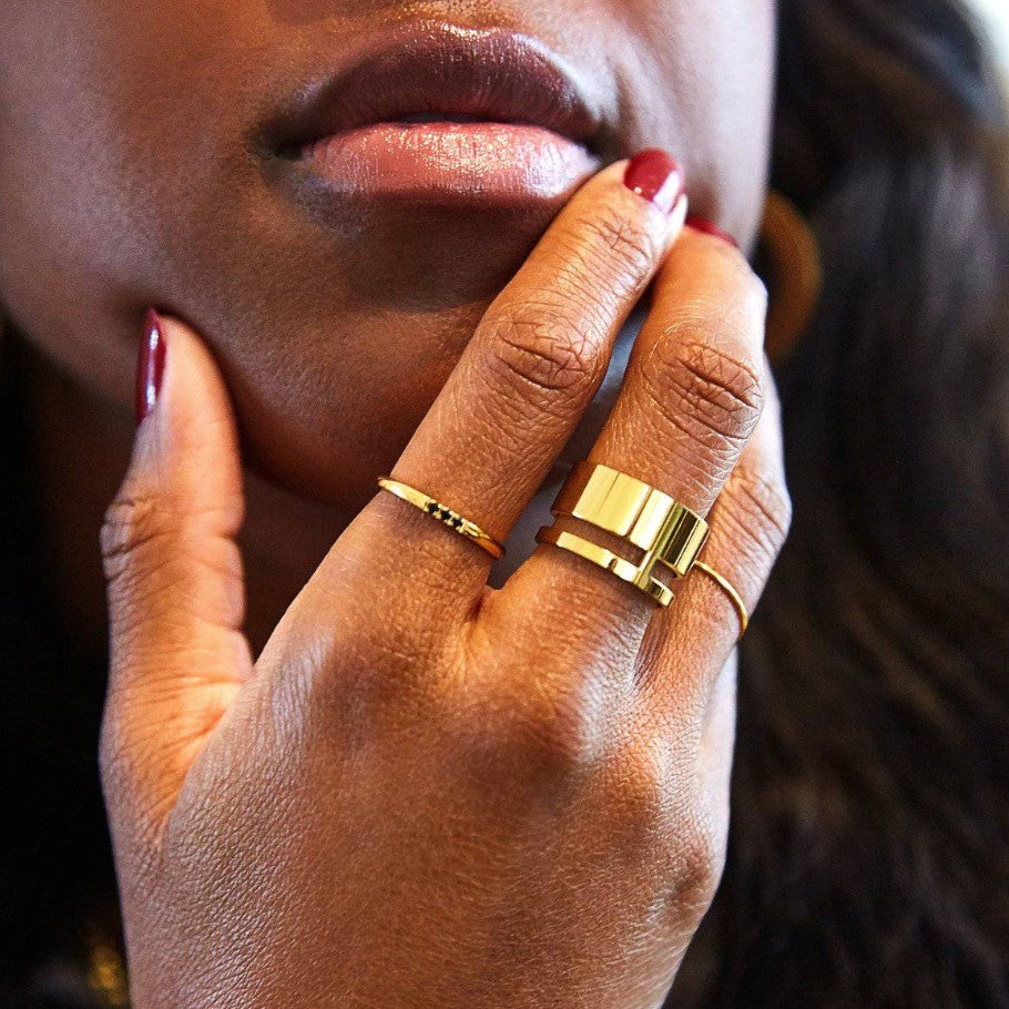 A person's hand wearing three gold rings of varying thickness.