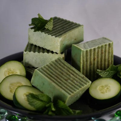 Several bars of soap stacked on top of each other surrounded by cucumbers