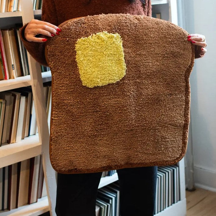 Small rug shaped like a piece of toast with a yellow pat of butter on it.