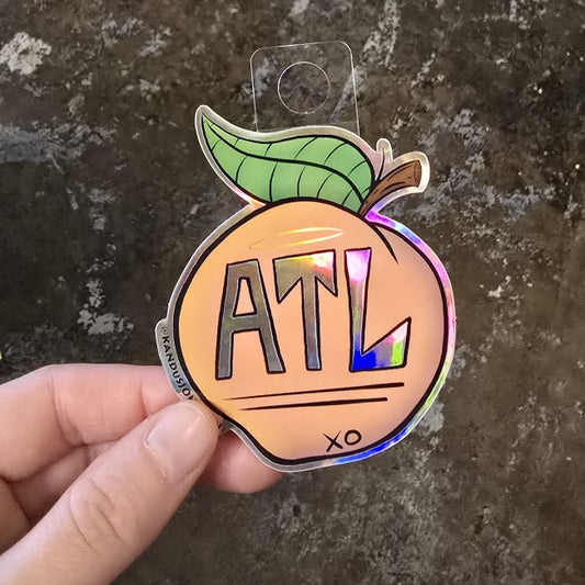 A small holographic peach sticker with 
"ATL" written on it in silver.