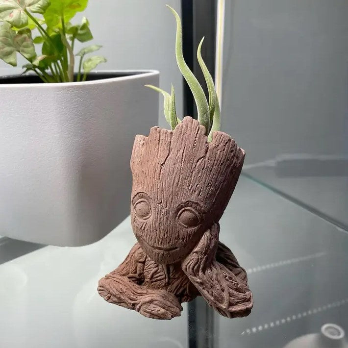 A small planter shaped like baby Groot propping his face in his hand.