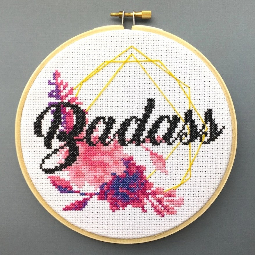 Cross-stitch hoop with a pink floral design and the word "badass" in cursive