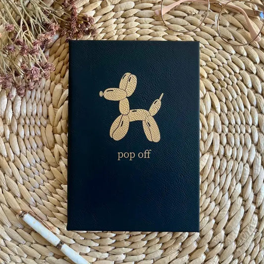 Black leather journal with an image of a balloon dog and the words "pop off" in gold on the cover