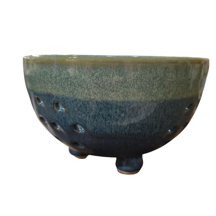 A blue and green speckled ceramic bowl with small feet on the bottom and small holes on the sides