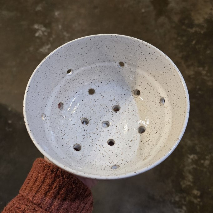 A white speckled pottery bowl with several circular holes along the bottom.