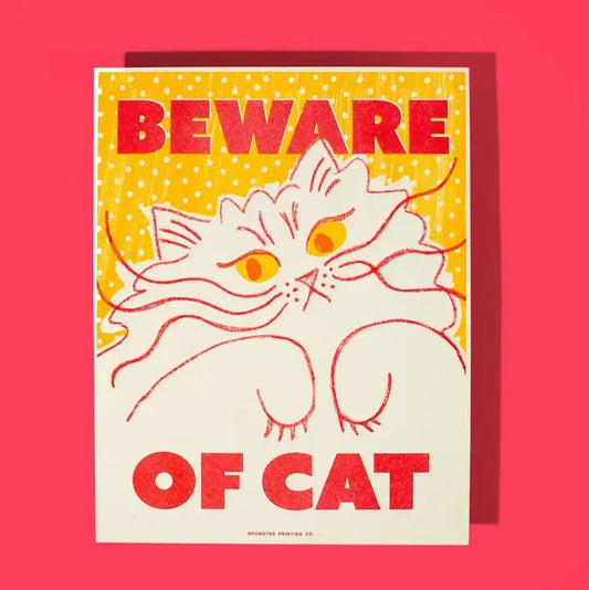 Risograph print of a fluffy white cat holding its paws up on a yellow polka dot background and red text "Beware of cat"