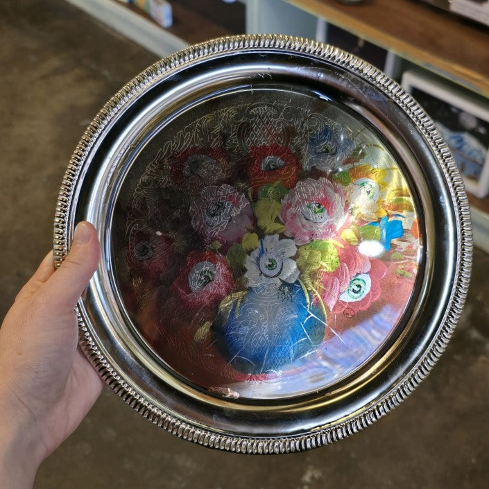 A silver metal tray with an image of a colorful bouquet with an eyeball at the center of every flower.