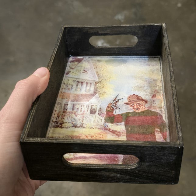 A small wooden tray with an image of Freddy Kreuger in front of a white Victorian style house.