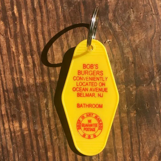 Yellow keychain with red text that reads "Bob's Burgers conveniently located on Ocean Avenue"