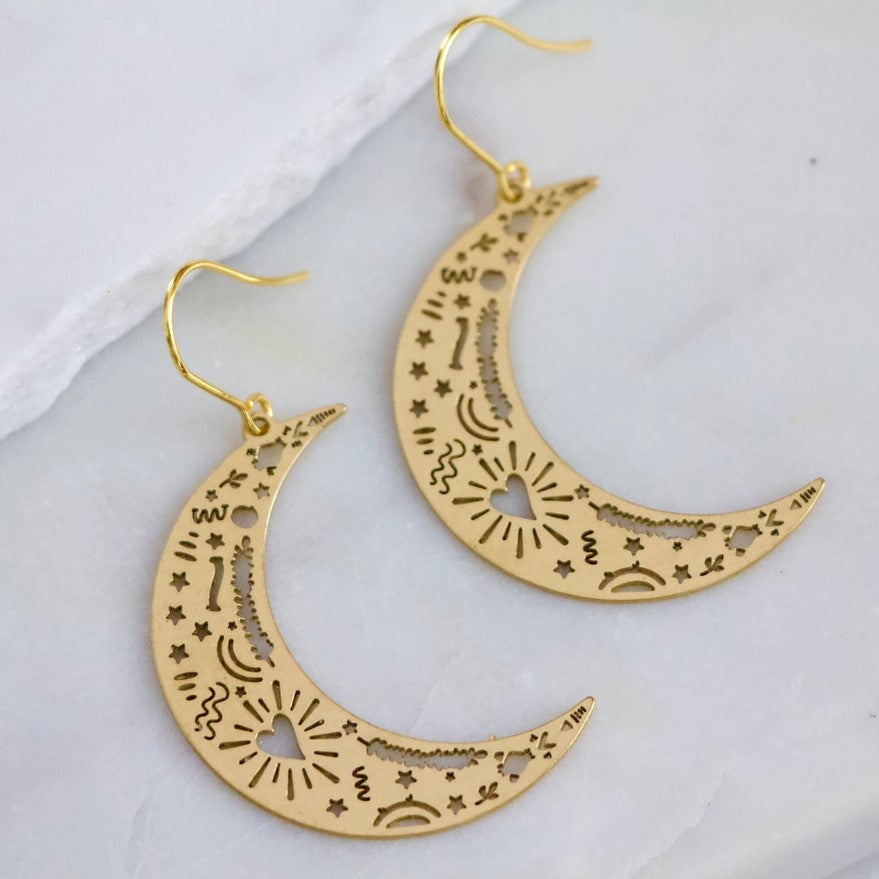 Dangling gold earrings shaped like crescent moons etched with hearts and squiggles