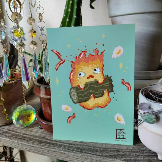 Small art print of a cartoon campfire with a worried face surrounded by eggs and bacon