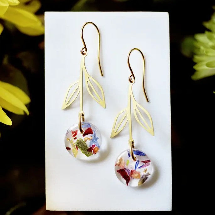 Gold earrings shaped like hanging flowers with charms filled with flower petals and gold leaf