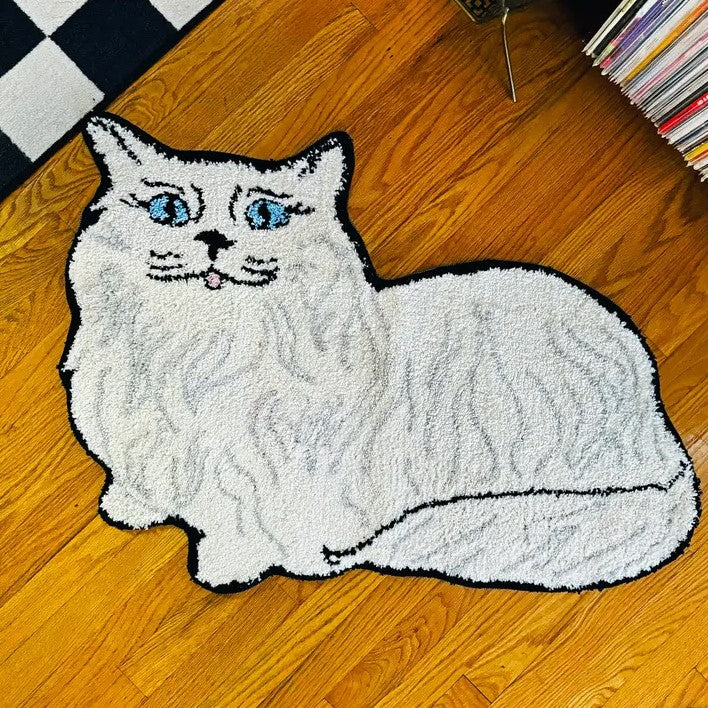 Small rug in the shape of a white Persian cat with blue eyes and a pink tongue lying down.