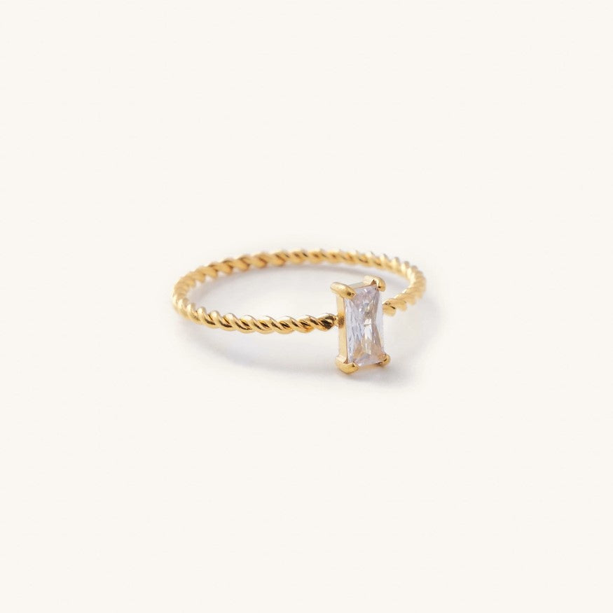 A delicate ring with a thin twisted gold band and a small rectangular white gemstone at the center.