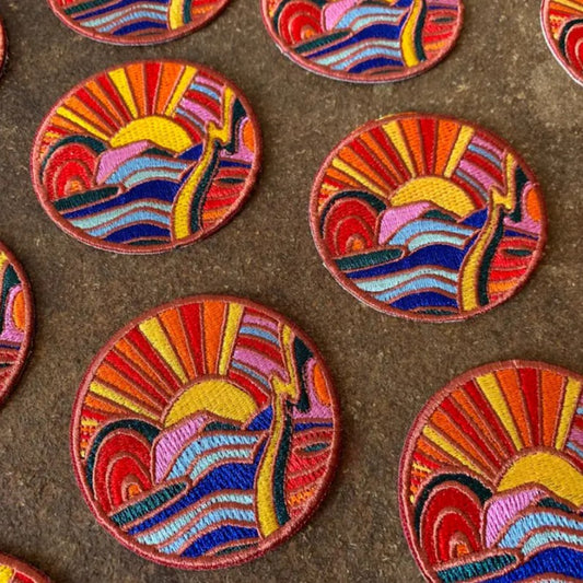 Circular iron-on fabric patches depicting colorful mountains and a sunset