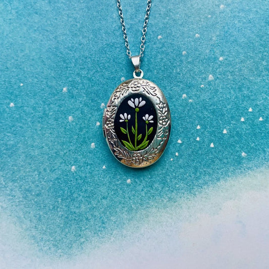 Silver oval locket with white flowers sculpted in clay on a black background 