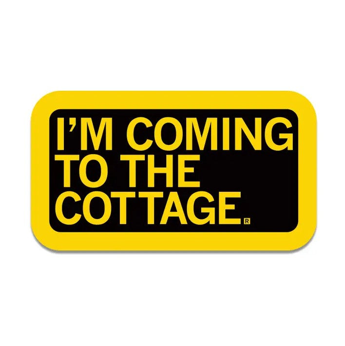 A rectangular black sticker with bright yellow text "I'm coming to the cottage."