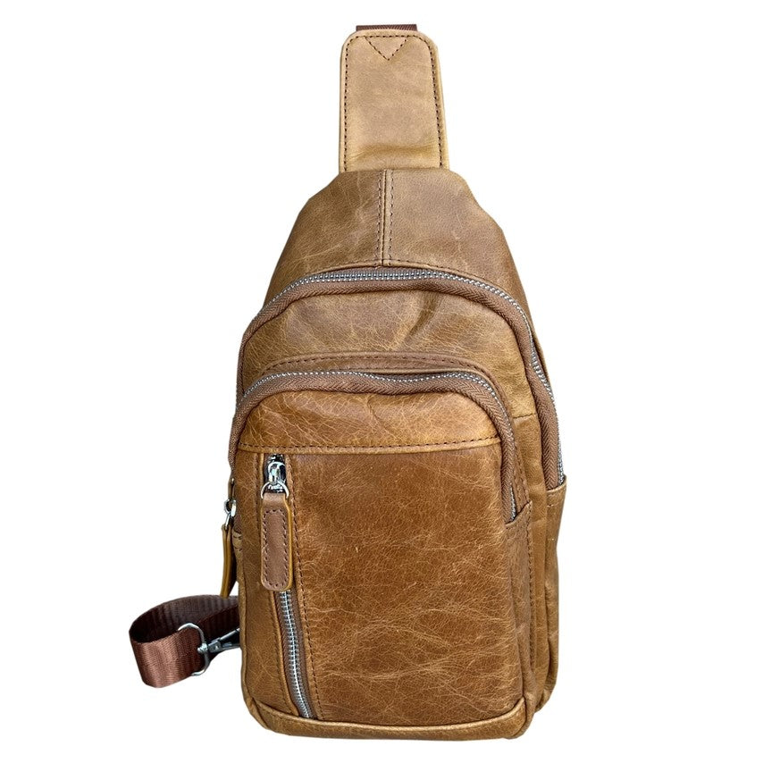 Front of a small tan leather crossbody bag with three zipper pockets on the front.