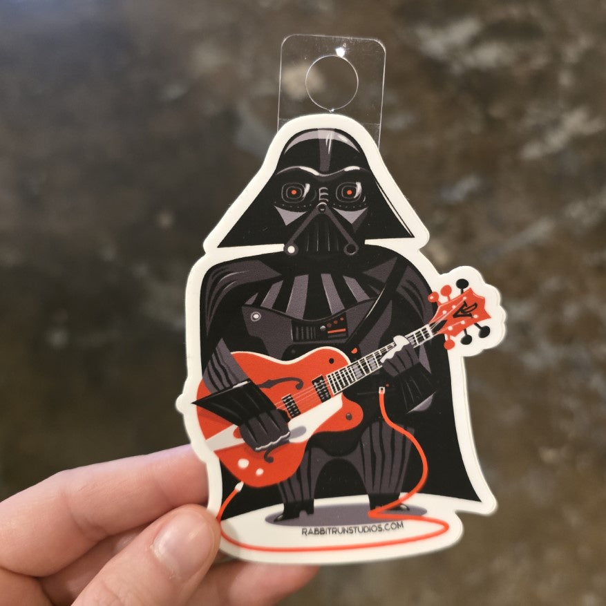 A sticker of a cartoon Darth Vader holding a red electric guitar.