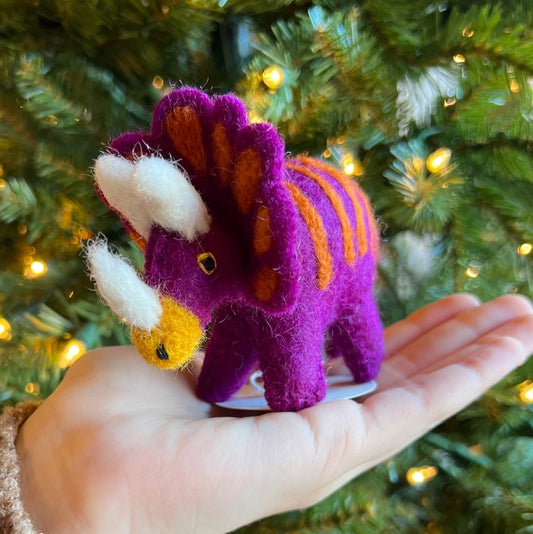 purple and orange dinosaur ornament held in front a christmas tree