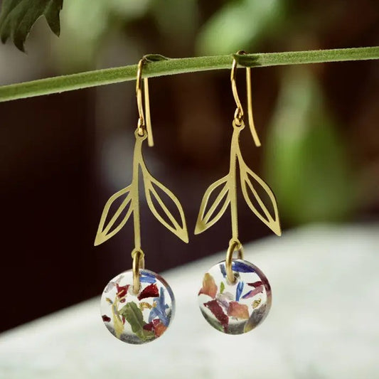 Gold earrings shaped like hanging flowers with charms filled with flower petals and gold leaf