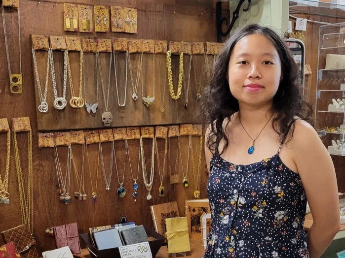 Artist Duo Wei in front of a shelf of resin and clay necklaces.