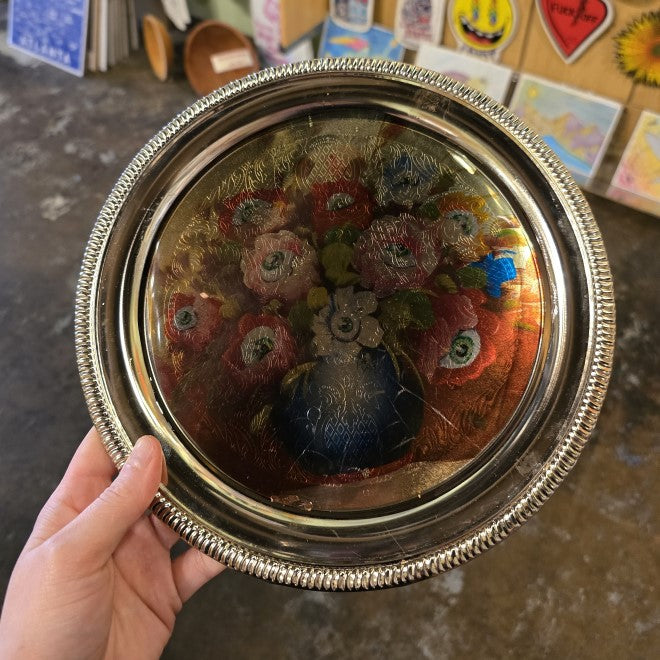 A silver metal tray with an image of a colorful bouquet with an eyeball at the center of every flower.