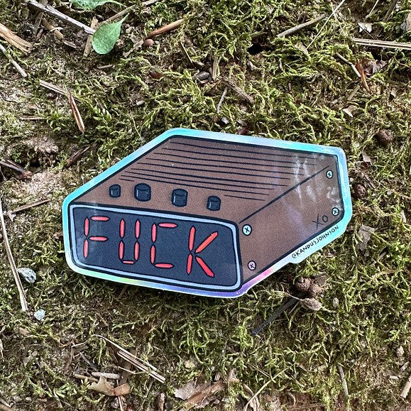 A small holographic sticker of an alarm clock with the time reading "FUCK"