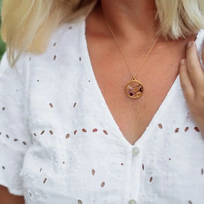 Model wearing a gold necklace in the shape of a moon with flowers set in resin