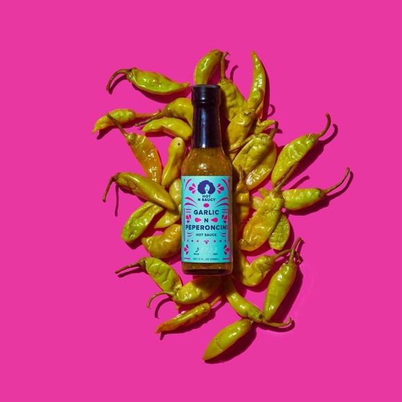 Bottle of garlic and pepperoncini hot sauce surrounded by pepperoncini's 