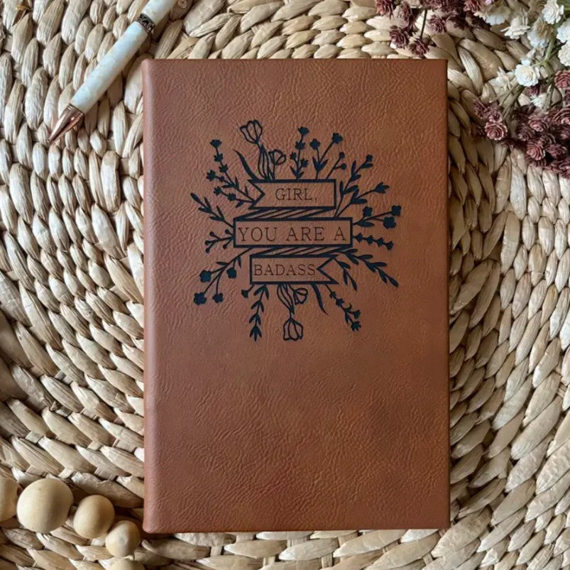 Brown leather journal with the words "Girl, you are a badass" surrounded by flowers on the cover