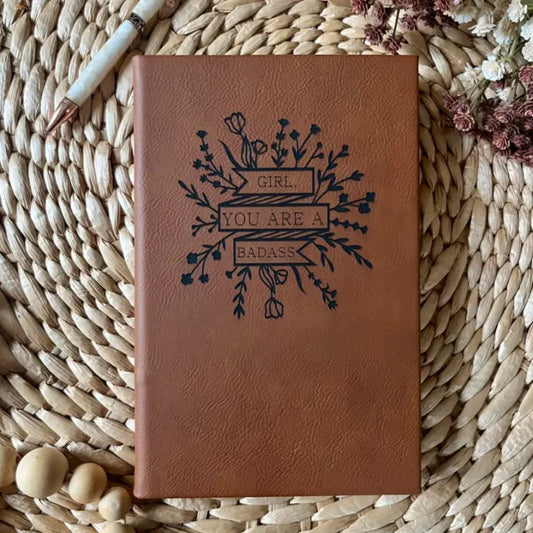 Brown leather journal with the words "Girl, you are a badass" surrounded by flowers on the cover