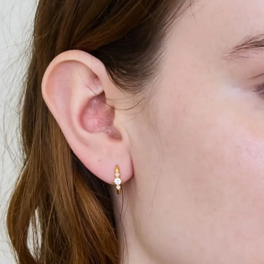 Person wearing dainty gold and crystal huggie earrings