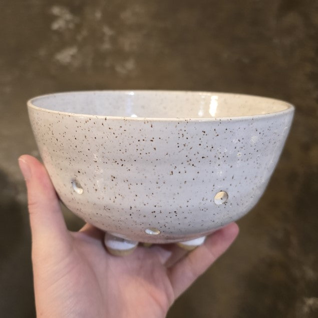 A white speckled pottery bowl with several circular holes along the bottom.